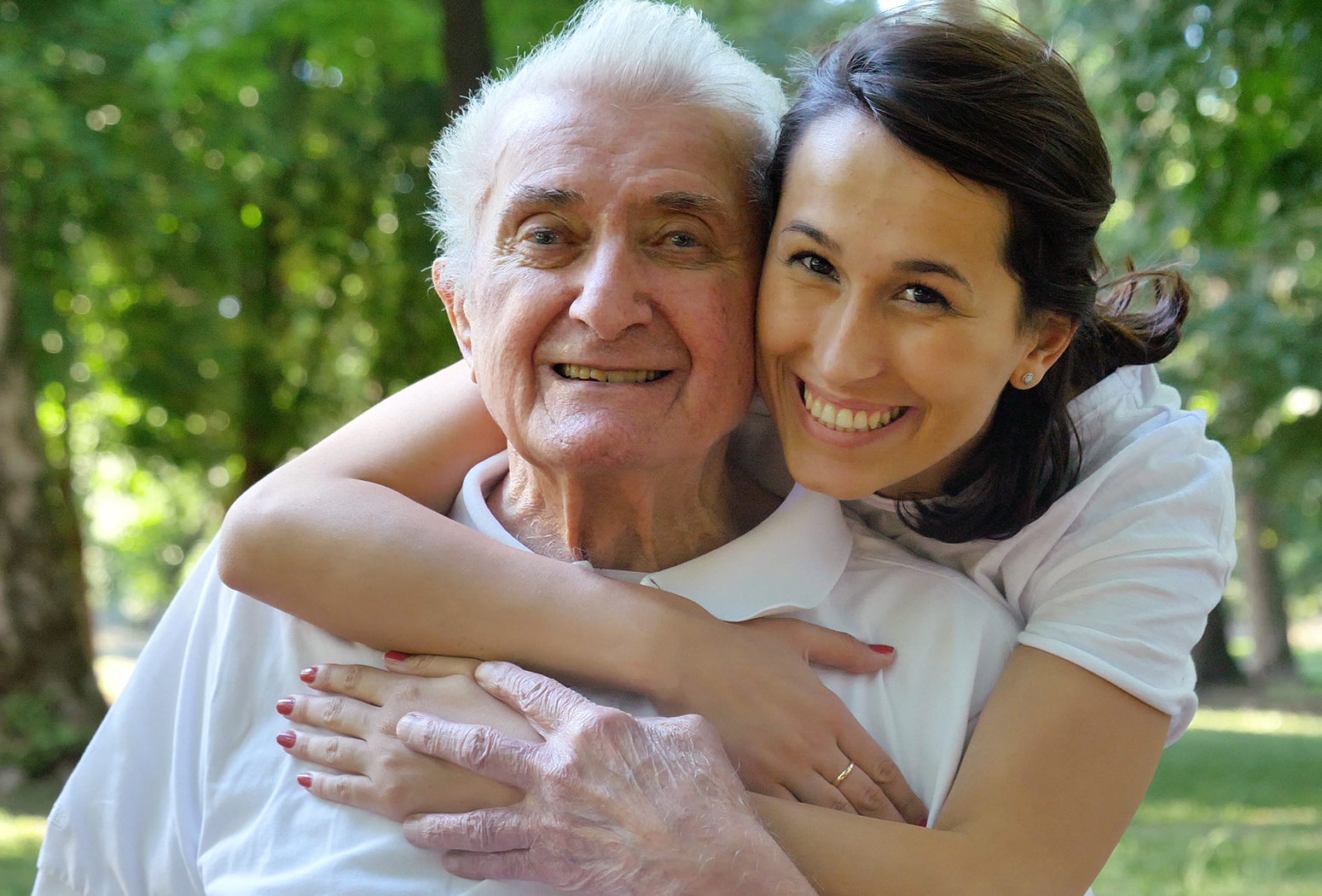 Smiling older man and woman in a park, embracing joyfully.